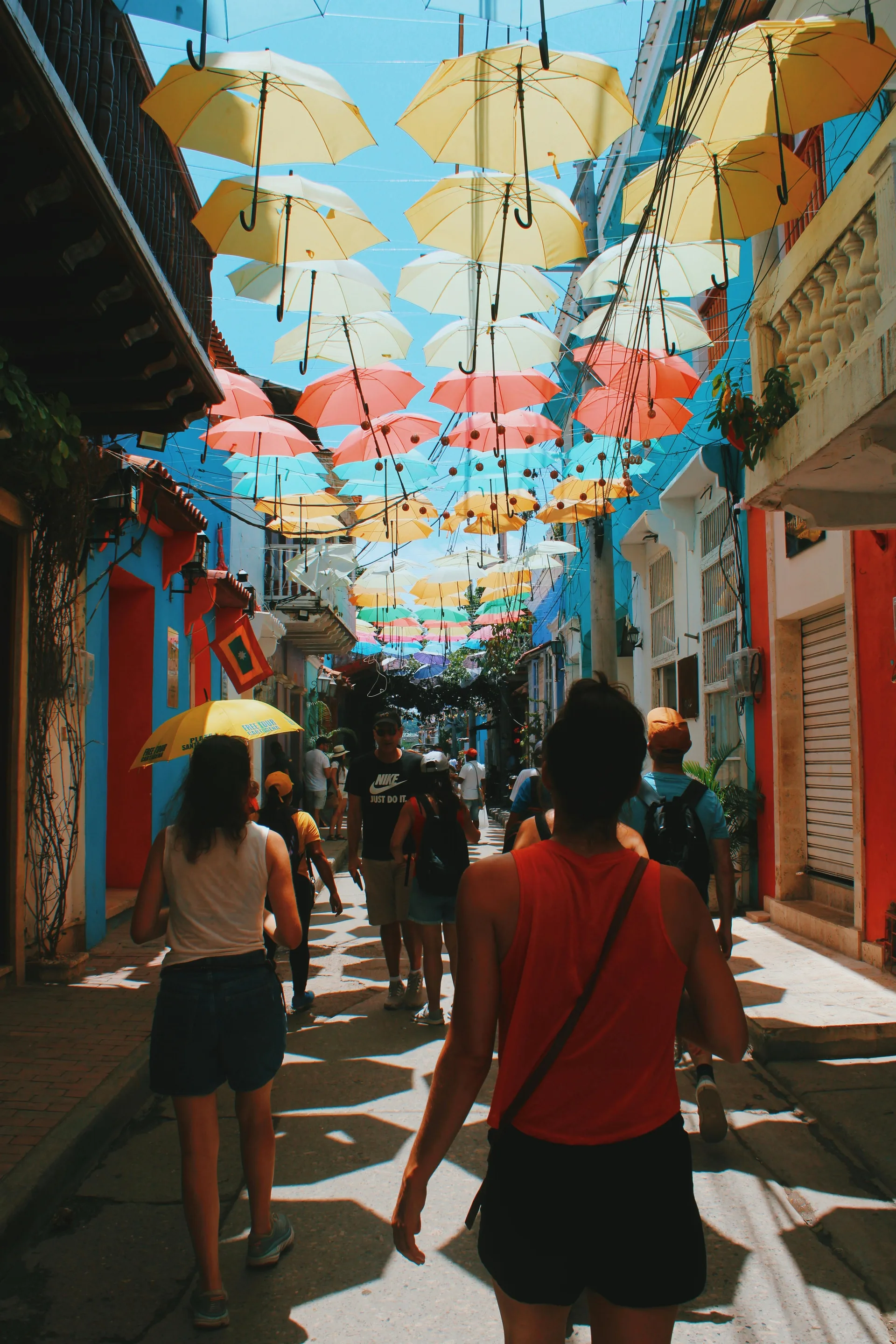 Tourists under the hanging umbrellas in Cartagena's old town, the kind of mid-year crowd the airport expects to push past 5,400 travelers a day during the World Cup season