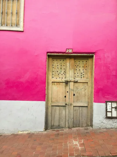 Colorful exterior of a building in Bogotá featuring a striking pink wall and rustic wooden door.