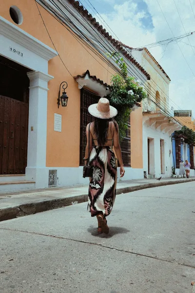 Fashionable woman in summer dress and hat strolling through historic Cartagena streets.