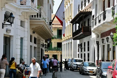 Vibrant street in a colonial town with people, cars, and balconies.