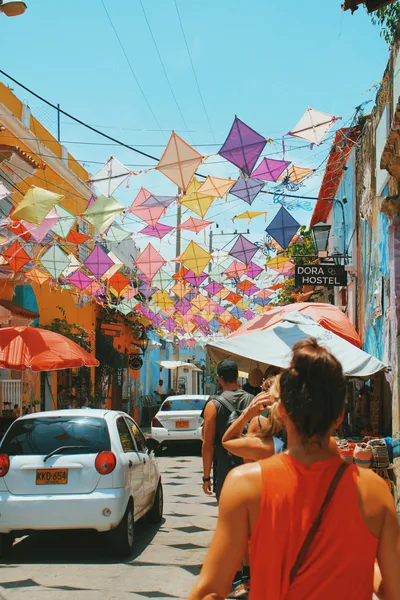 Tourists walk under colorful kites in a vibrant street of Cartagena, Colombia, capturing the lively urban atmosphere.